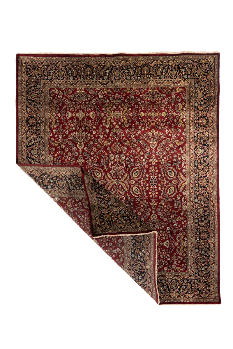 Alfombra roja de estilo persa con una esquina levantada que deja ver el reverso y el espesor del tejido.