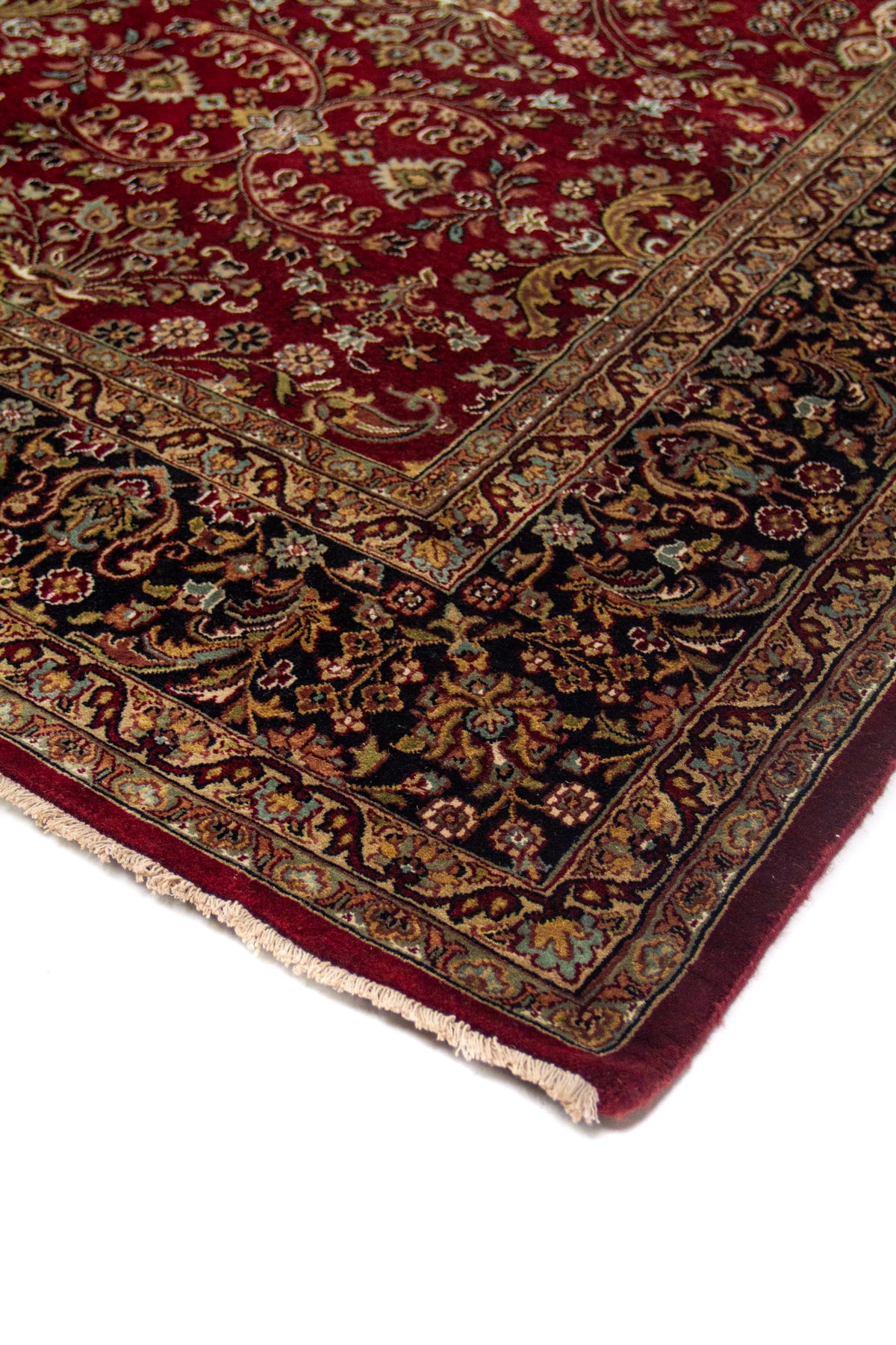 Detalle en perspectiva de alfombra roja con borde azul oscuro, motivos florales y terminación con flecos