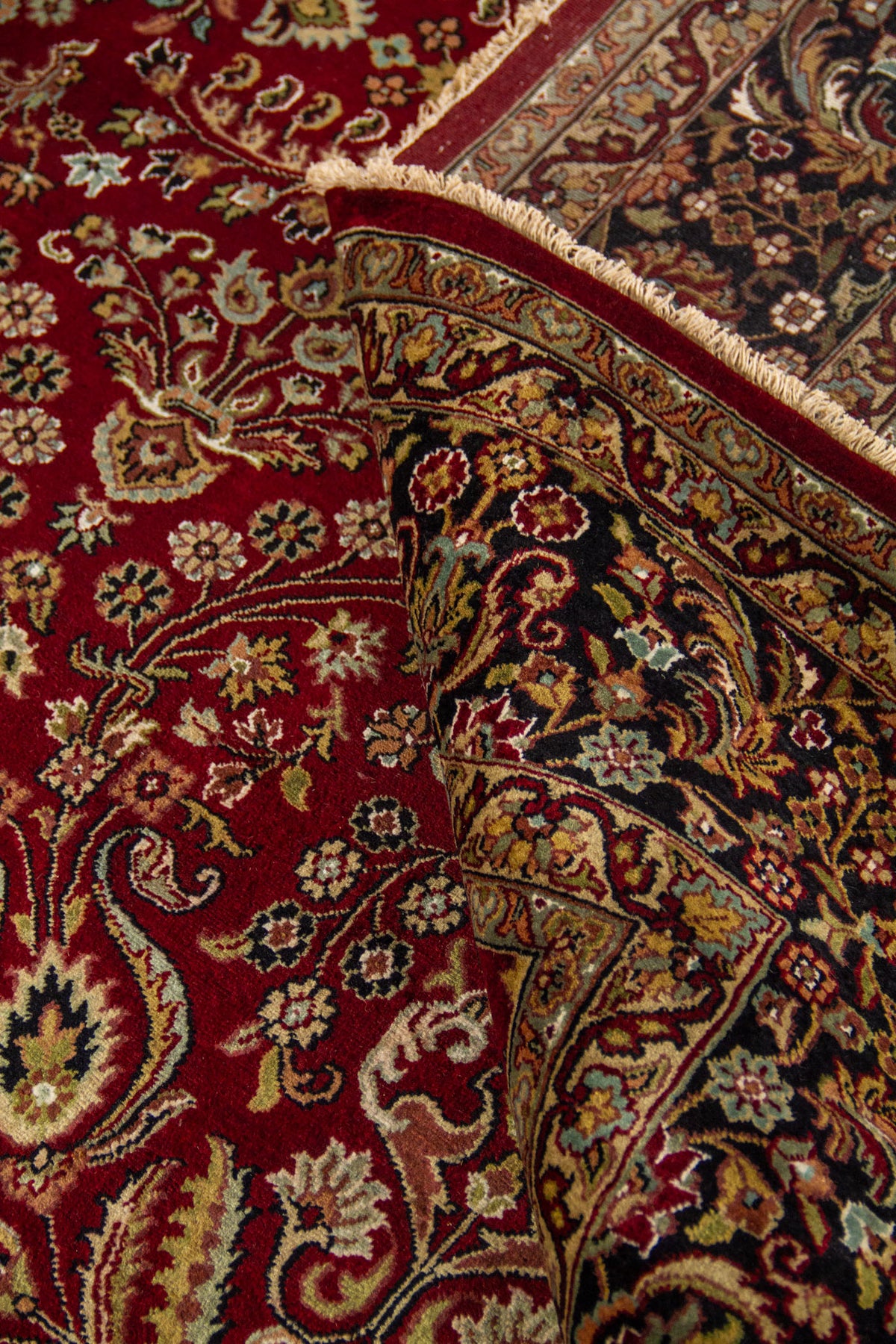 Alfombra roja doblada mostrando su flexibilidad, textura y detalles florales en el campo central y la guarda.