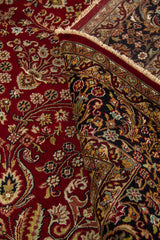 Alfombra roja doblada mostrando su flexibilidad, textura y detalles florales en el campo central y la guarda.