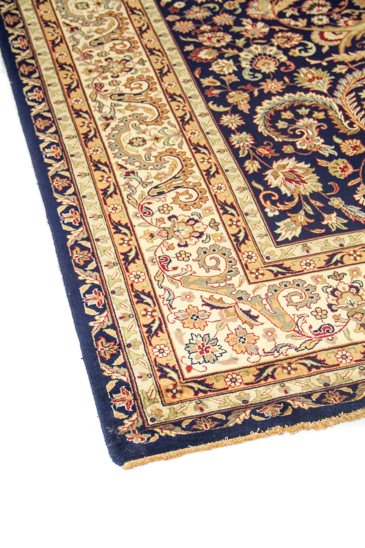 Detalle lateral de alfombra oriental azul oscuro con cenefas beige y diseño floral elegante