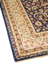 Detalle lateral de alfombra oriental azul oscuro con cenefas beige y diseño floral elegante