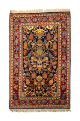 Vista superior de una alfombra oriental con fondo azul oscuro, adornada con un diseño floral simétrico y un gran jarrón central, rodeada por un borde rojo con motivos florales.