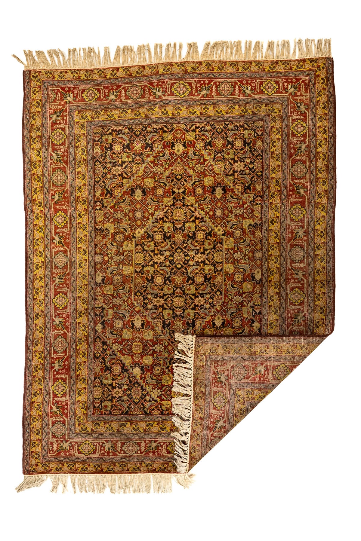 Alfombra oriental con una esquina doblada, mostrando el reverso del tejido y la riqueza del patrón en tonos cálidos y detalles florales simétricos.