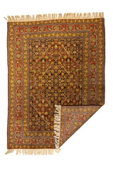 Alfombra oriental con una esquina doblada, mostrando el reverso del tejido y la riqueza del patrón en tonos cálidos y detalles florales simétricos.