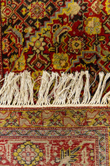 Detalle cercano de los flecos y el borde inferior de una alfombra oriental, con motivos florales sobre fondo rojo intenso y amarillo mostaza.