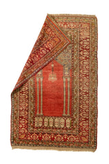 Alfombra con una esquina doblada, mostrando el reverso y destacando el diseño de columnas y el motivo de lámpara central sobre un fondo rojo.