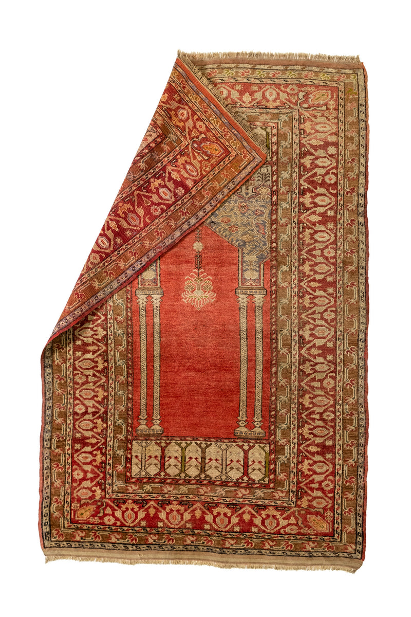 Alfombra con una esquina doblada, mostrando el reverso y destacando el diseño de columnas y el motivo de lámpara central sobre un fondo rojo.