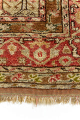Plano cercano del borde inferior de la alfombra, con motivos florales en tonos marrón, rojo y verde, mostrando la densidad del tejido.