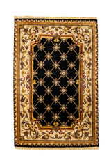 Vista completa superior de una alfombra clásica con fondo negro, patrón de rombos beige con flores en el cruce, y un borde ornamentado en tonos dorados, burdeos y beige.