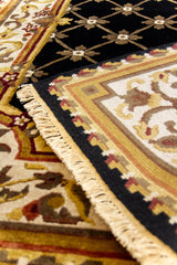 Detalle cercano del borde de una alfombra negra con diseño floral geométrico, resaltando los flecos y la calidad del entramado artesanal.