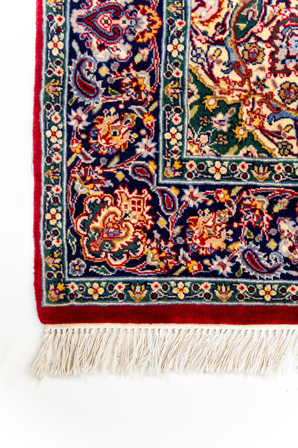 Esquina inferior de la alfombra con flecos beige y borde azul con motivos florales.
