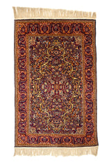 Alfombra rectangular con fondo burdeos y diseño floral intrincado en tonos dorados, azules y naranjas, con flecos en los extremos.