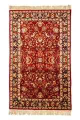 Alfombra extendida con diseño floral simétrico sobre fondo rojo y borde beige con detalles azul oscuro.