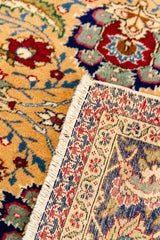 Detalle del reverso de una alfombra mostrando los nudos finos y el patrón artesanal en tonos rojo, azul y beige.