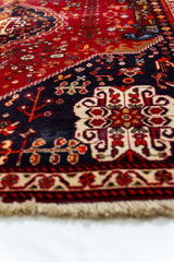 Detalle en perspectiva baja de la alfombra persa, enfocando los patrones florales sobre fondo azul marino y rojo profundo.