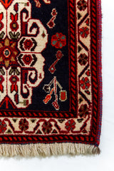 Primer plano del borde de la alfombra persa, mostrando el entramado floral en beige, rojo y azul oscuro.