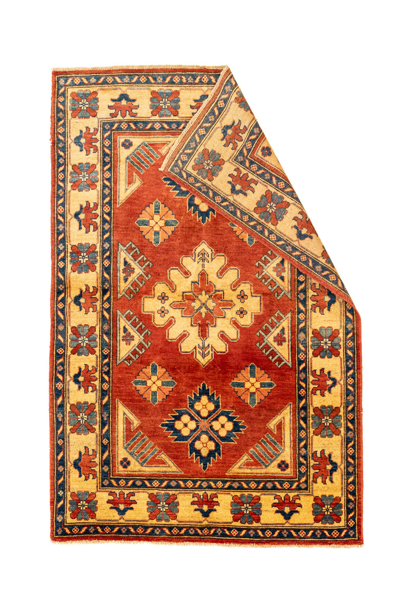 Alfombra con una esquina doblada mostrando el reverso y los detalles simétricos de su diseño tradicional.