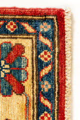Detalle del borde de una alfombra con trama visible y patrón floral en tonos azul, rojo y beige.