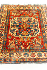 Vista inclinada de alfombra oriental que resalta los detalles del medallón central azul y los patrones simétricos en tonos cálidos.