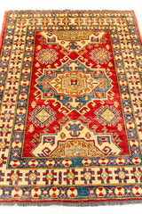 Vista angular de la alfombra oriental que resalta el diseño central simétrico y el contraste vibrante entre los colores rojo, azul y beige.