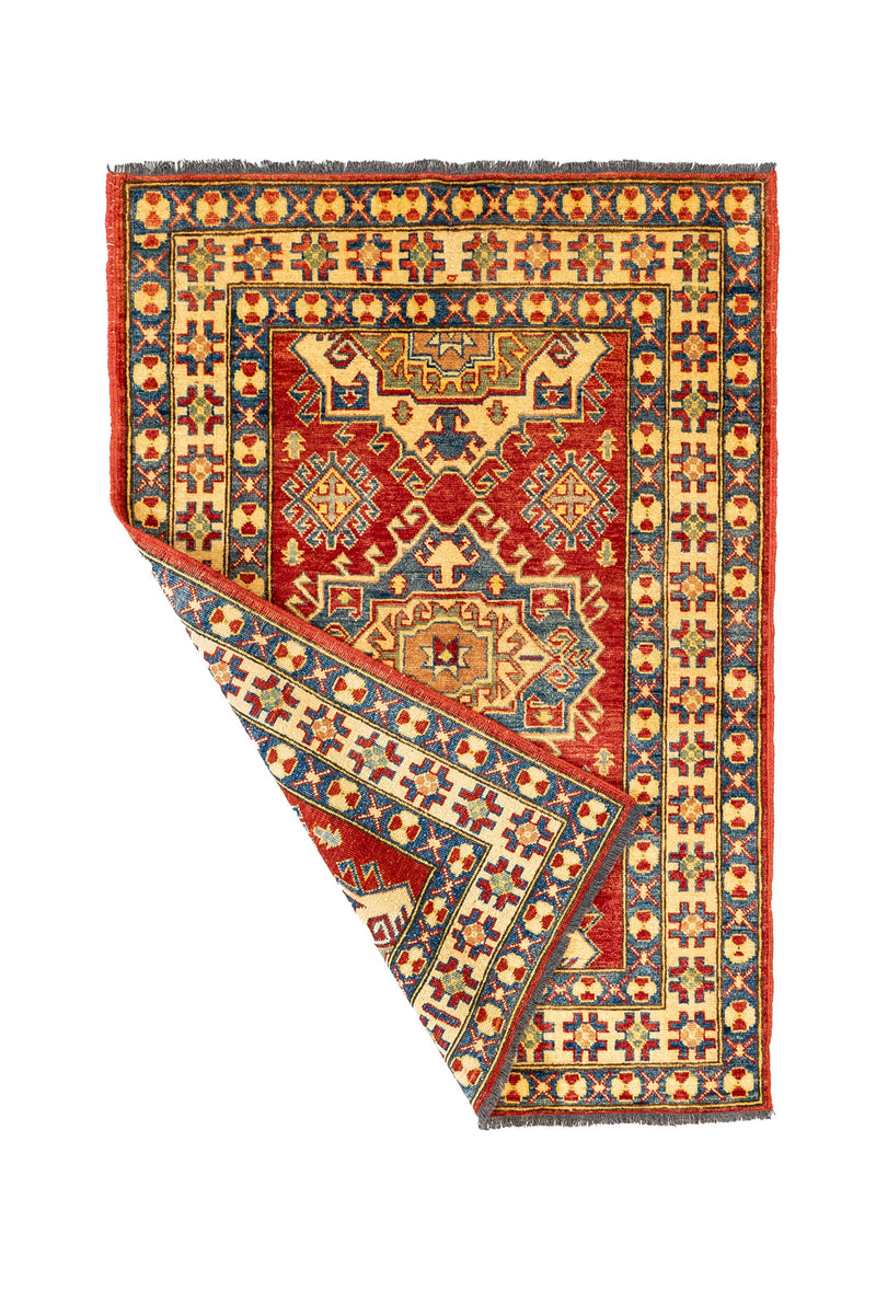 Alfombra oriental parcialmente doblada, mostrando el reverso tejido y los detalles precisos del borde decorativo.