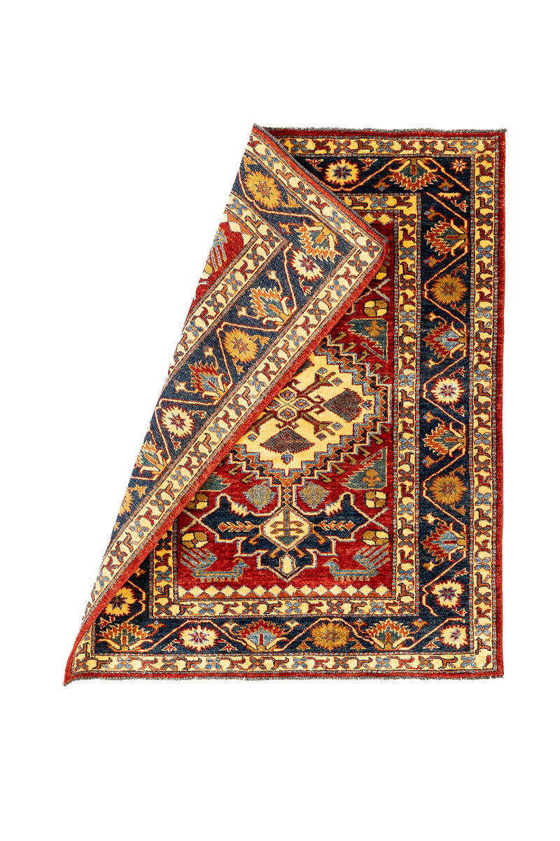 Alfombra parcialmente doblada que deja ver el reverso tejido y resalta los colores vibrantes y la estructura del borde decorativo.