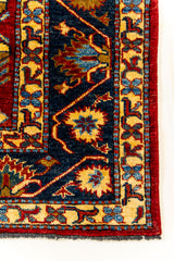 Primer plano del borde de la alfombra, mostrando el detalle artesanal de los motivos florales en azul y crema sobre un fondo oscuro.