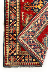 Primer plano del doblez de la alfombra, centrado en los patrones del borde y los detalles del reverso en rojo, azul y beige.