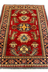 Vista angular de la alfombra oriental, que resalta el diseño central y los colores vibrantes del rojo, azul marino, dorado y beige.