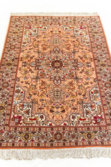 Primer plano en ángulo de una alfombra oriental con fondo rosado y medallón central geométrico en tonos marrón y beige.