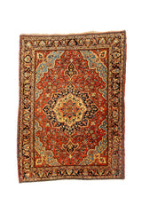 Alfombra con fondo rojo y medallón central en tonos beige, azul oscuro y dorado, rodeado por un denso patrón floral y una guarda decorativa en negro y beige.
