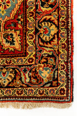 Primer plano del borde inferior derecho de la alfombra, mostrando los detalles de la guarda negra con flores estilizadas en azul, rojo y dorado.