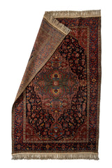 Alfombra persa con esquina doblada mostrando el reverso del tejido y el diseño central en tonos terracota, azul oscuro y verde.