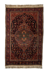 Vista completa de alfombra persa antigua con medallón central simétrico en tonos cálidos sobre fondo rojo y azul oscuro.