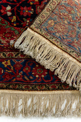 Primer plano del fleco y borde de la alfombra persa, destacando el reverso del tejido en azul y rojo con patrón floral.