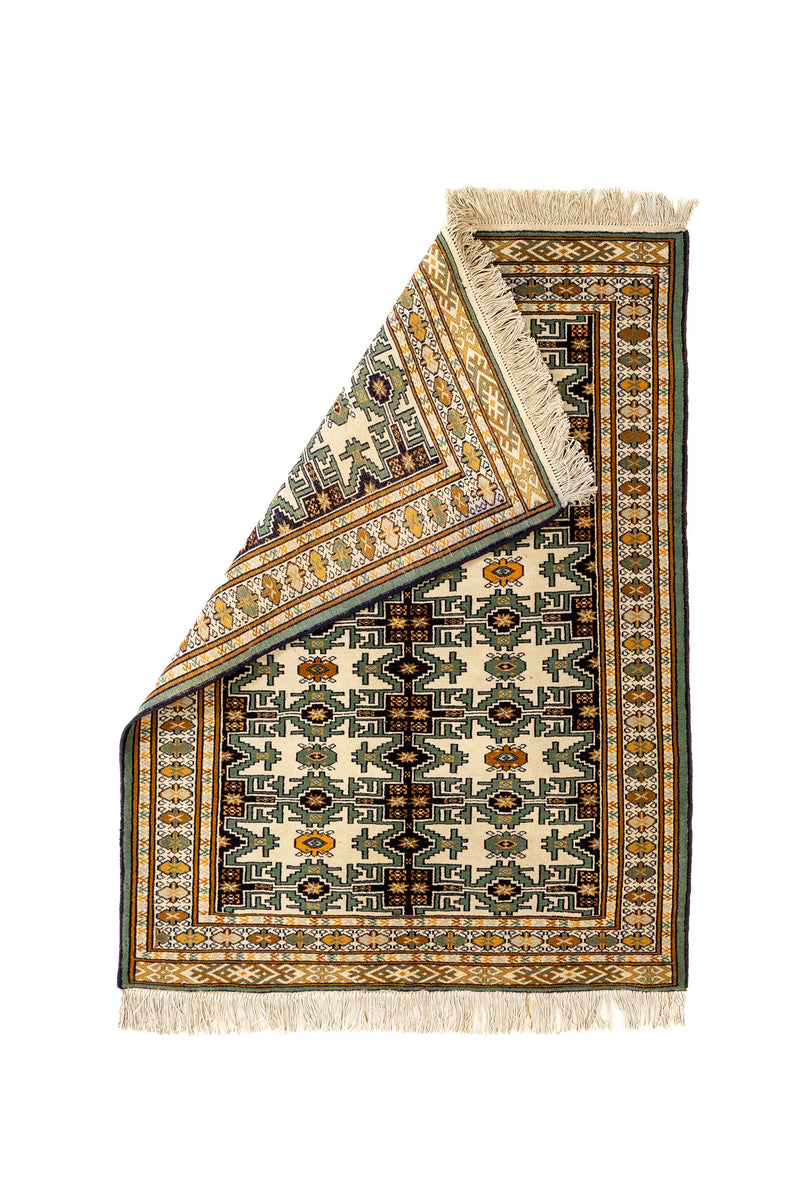 Alfombra doblada en una esquina, mostrando el reverso del tejido y el entramado de su diseño tradicional.