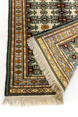 Detalle del borde inferior izquierdo con flecos visibles y colores tierra en los marcos de la alfombra.