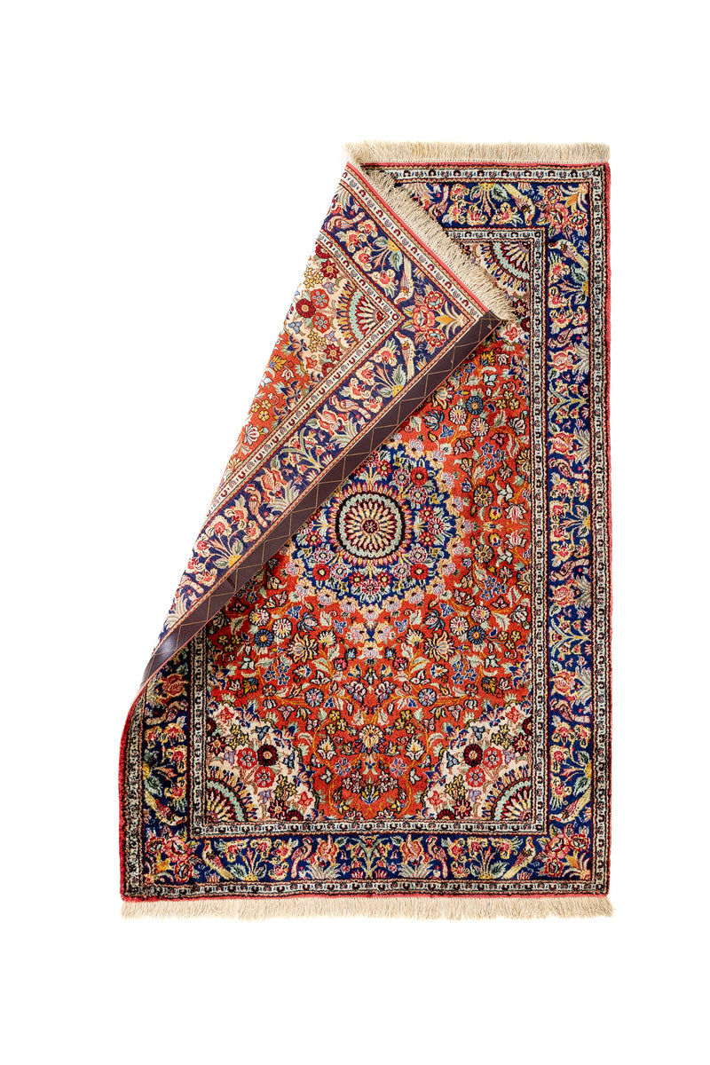 Alfombra doblada desde una esquina para mostrar el reverso y los detalles del borde y flecos.