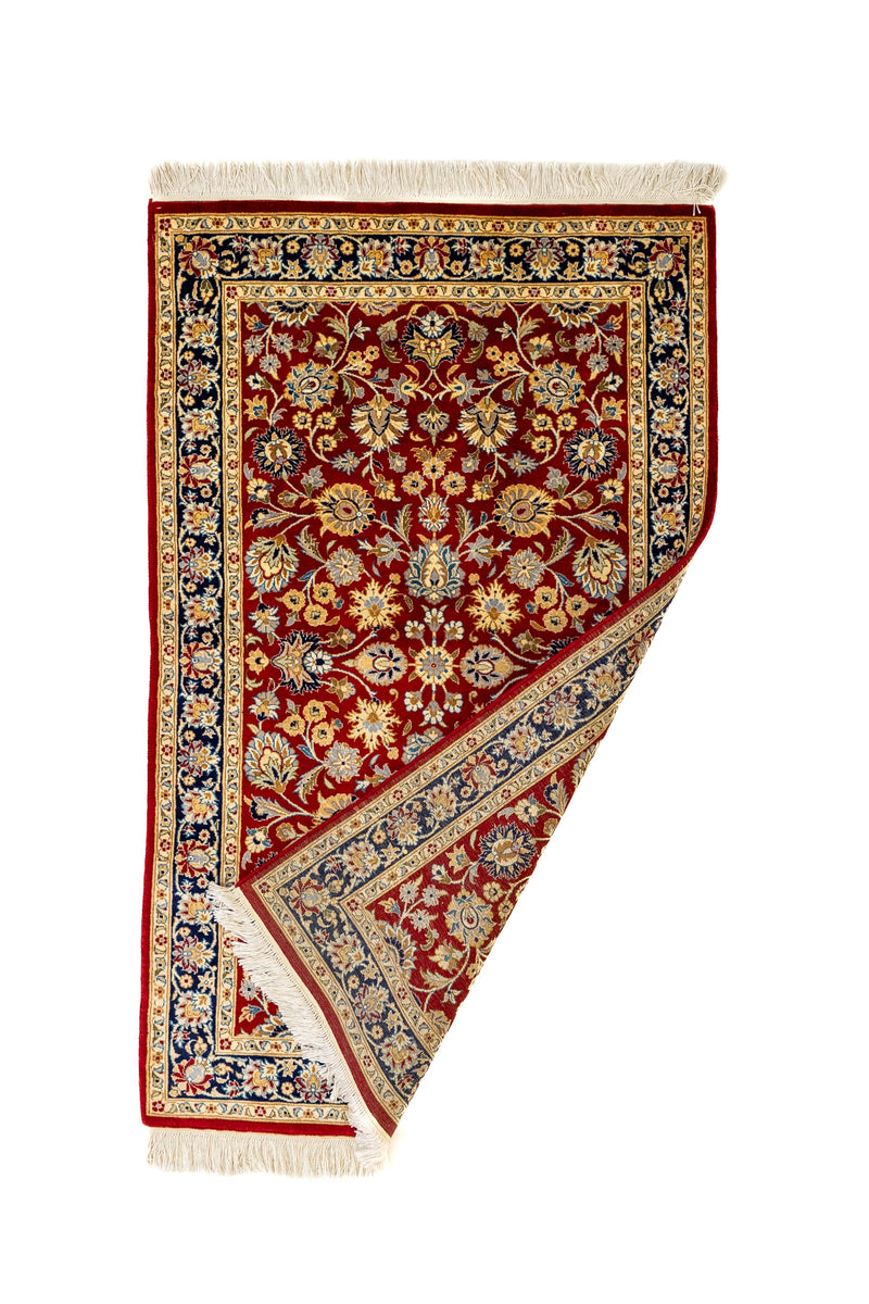 Detalle de la esquina doblada mostrando el reverso de la alfombra roja con diseño floral intrincado y bordes decorados en azul.