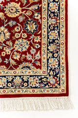 Plano detalle del borde inferior derecho de la alfombra con flores beige sobre fondo azul marino y flecos blancos.