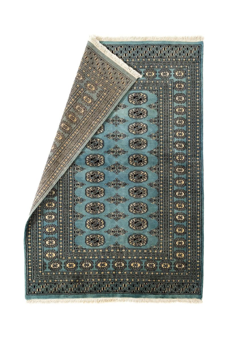 Alfombra Bukhara parcialmente doblada, mostrando la parte posterior tejida a mano y los detalles precisos del borde decorativo.