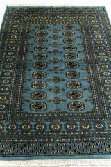 Perspectiva en ángulo de la alfombra Bukara extendida, con patrones octogonales centrales y marco compuesto por franjas finas y florales.