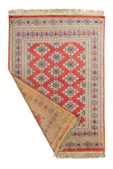 Alfombra artesanal parcialmente doblada mostrando el reverso tejido a mano con colores tierra y diseño simétrico.