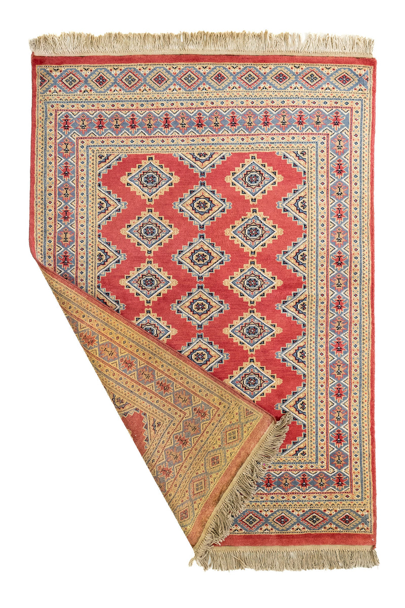 Alfombra artesanal parcialmente doblada mostrando el reverso tejido a mano con colores tierra y diseño simétrico.