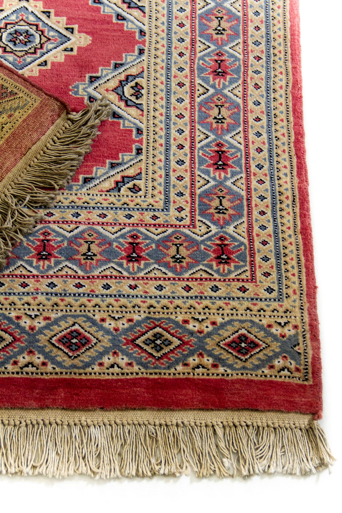 Primer plano de la esquina inferior derecha de la alfombra, destacando la guarda con motivos florales y los flecos decorativos.