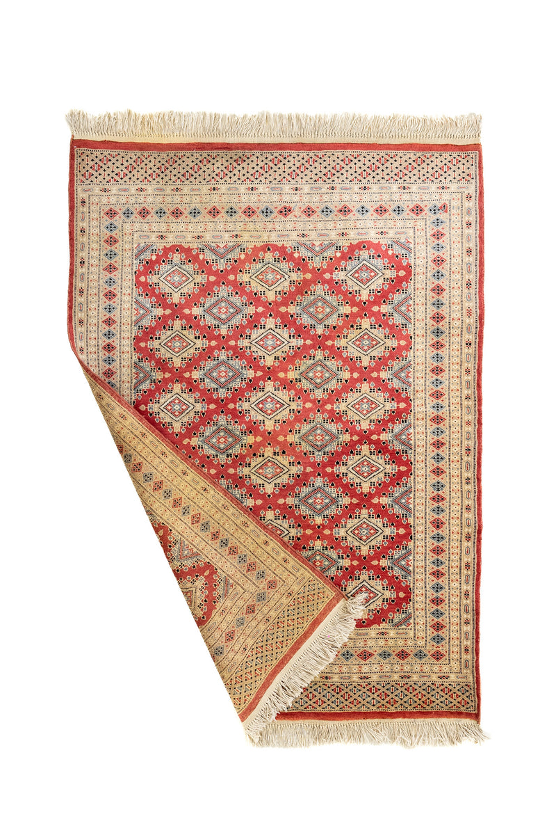 Alfombra doblada mostrando tanto el anverso como el reverso, con detalles de tejido tradicional y flecos decorativos.