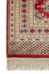 Detalle de la esquina inferior izquierda de la alfombra, enfocando el borde beige con motivos en diamante y la textura del tejido.