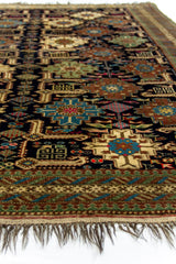 Vista en perspectiva de la alfombra mostrando la textura de los nudos y los motivos geométricos en azul y beige sobre fondo oscuro.