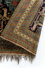 Detalle del reverso de la alfombra mostrando el entramado del tejido en colores tierra, con anillos de sujeción metálicos cosidos al borde.